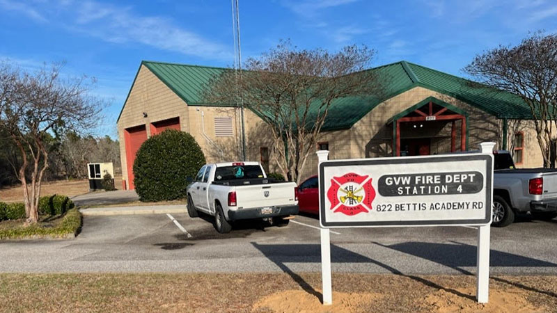 A beige fire station with a green roof, labeled "GVW Fire Dept Station 4, 822 Bettis Academy Rd." Two pickup trucks are parked in front, and the area is surrounded by trees and a clear blue sky.
