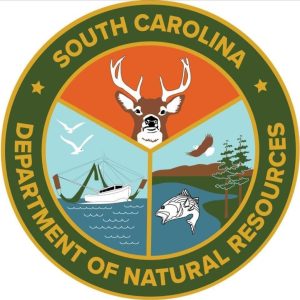 Logo of the South Carolina Department of Natural Resources, featuring sections with a deer, a fishing boat on water, and a fish with trees and a bird. It is circular with green and orange colors.